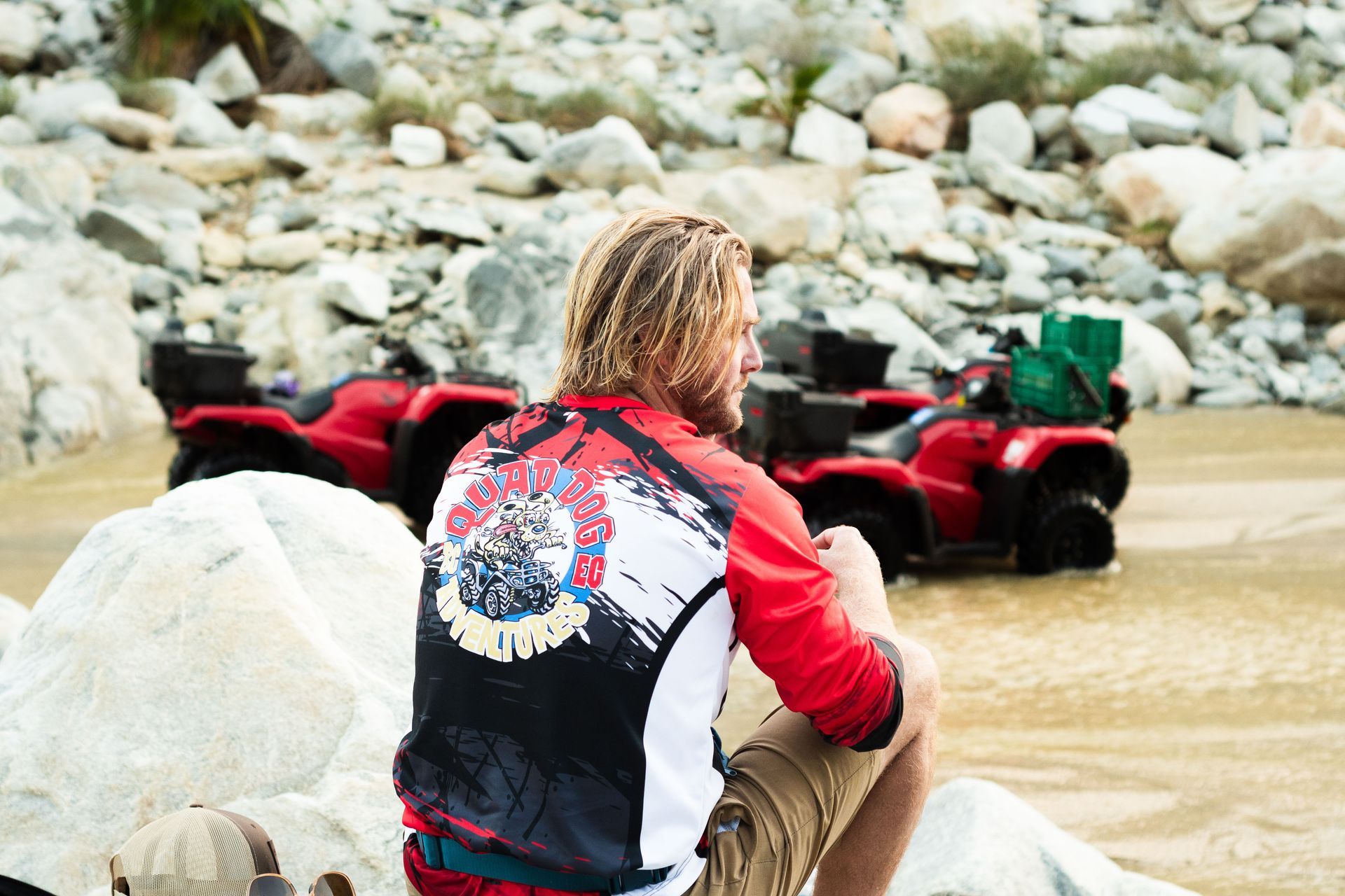 A man is sitting on a rock in front of two atvs.