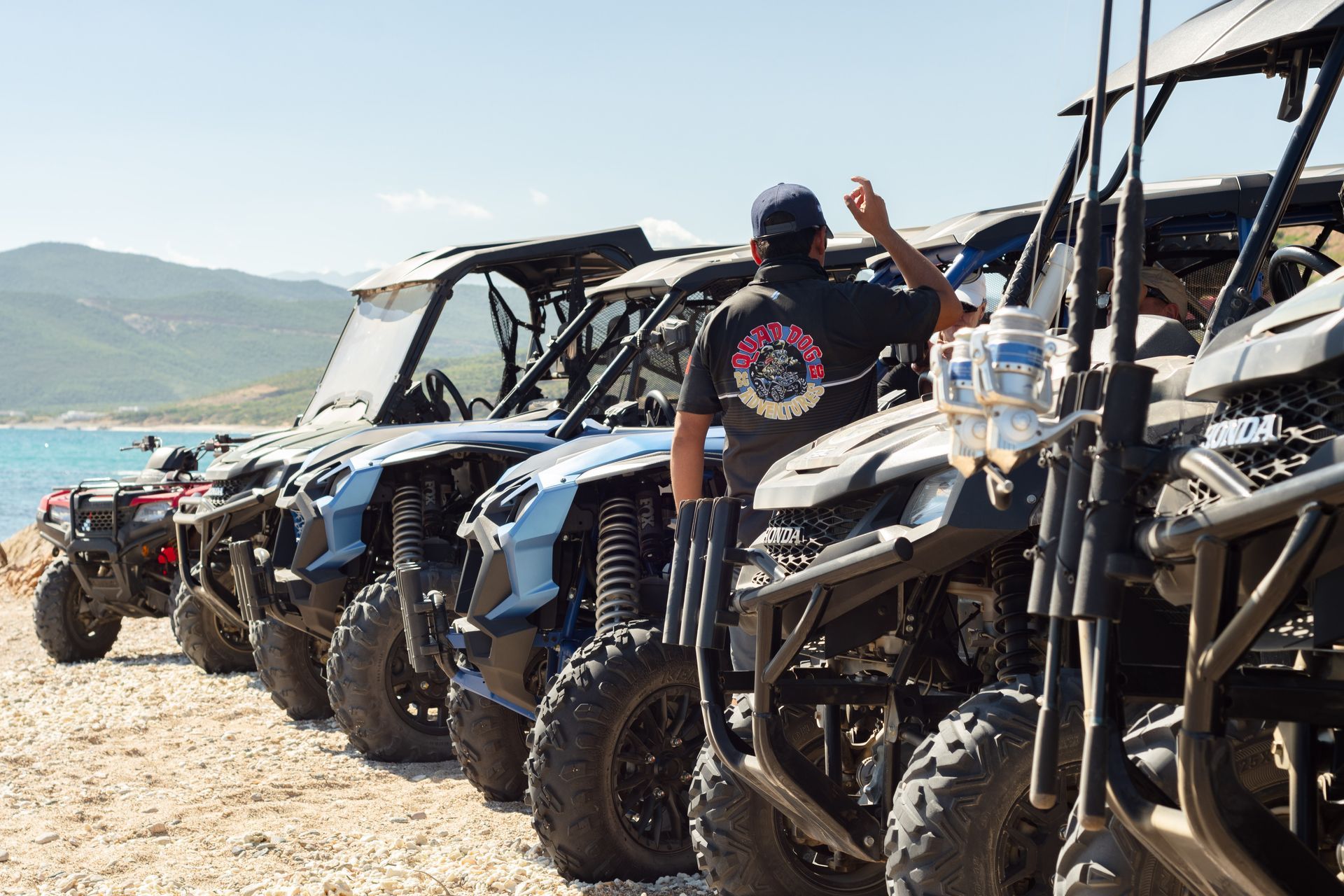 A man is standing in front of a row of atv 's on the beach.