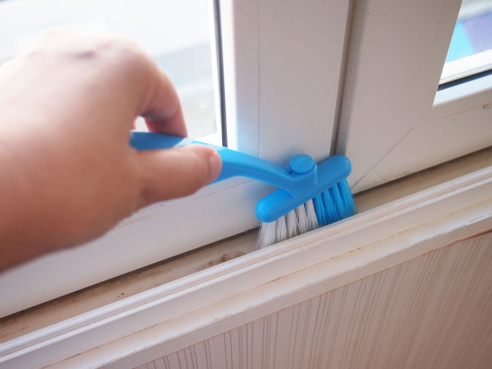 A Person is Cleaning a Window With a Blue Brush — Reach 'N' Clean in Byron Bay, NSW