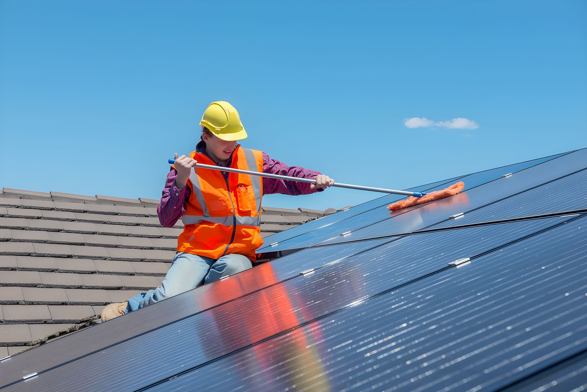 A Man is Cleaning Solar Panels on the Roof of a House — Reach 'N' Clean in Lismore, NSW