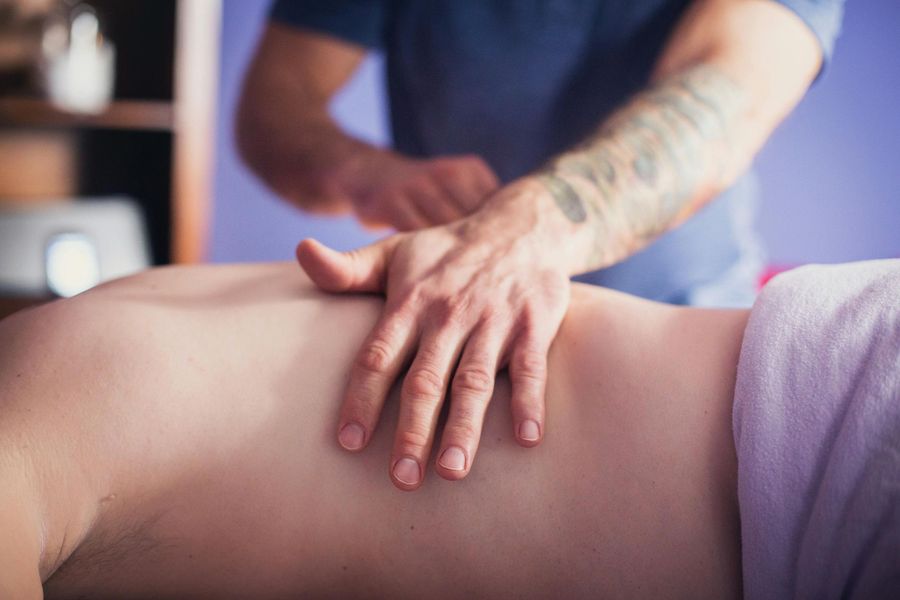 Person receiving a back massage; therapist's tattooed arm and hand on client's back.