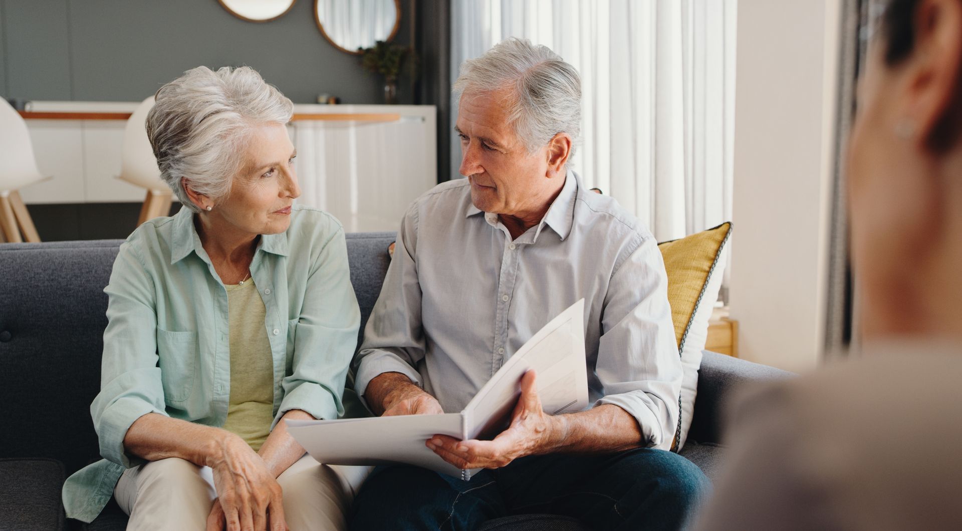 An elderly couple is sitting on a couch looking at a piece of paper.