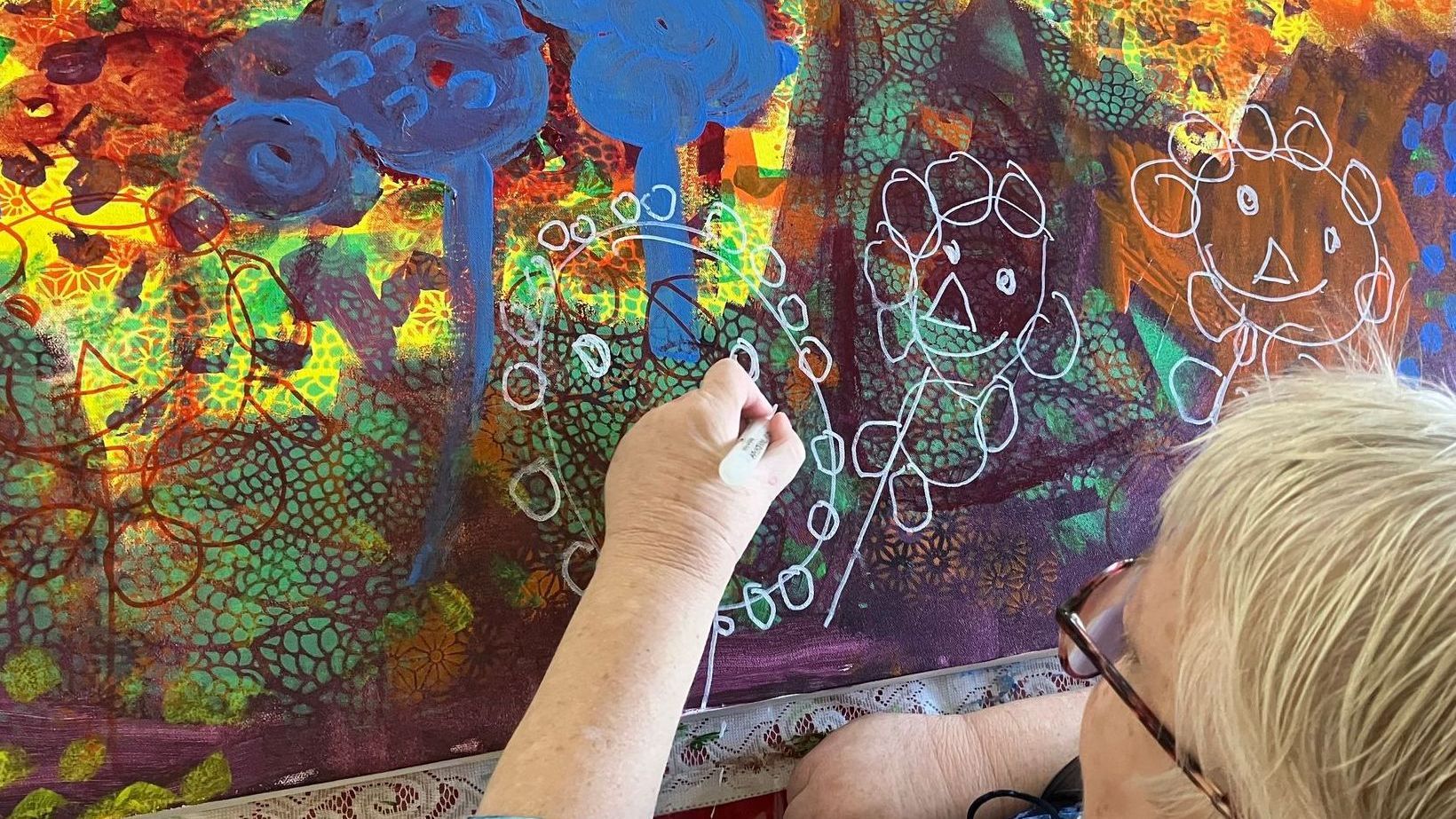 Darlene drawing flowers on painted canvas