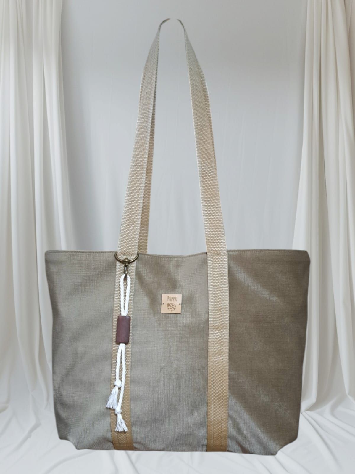 Una bolsa de mano gris con una correa de color canela se encuentra sobre una tela blanca.