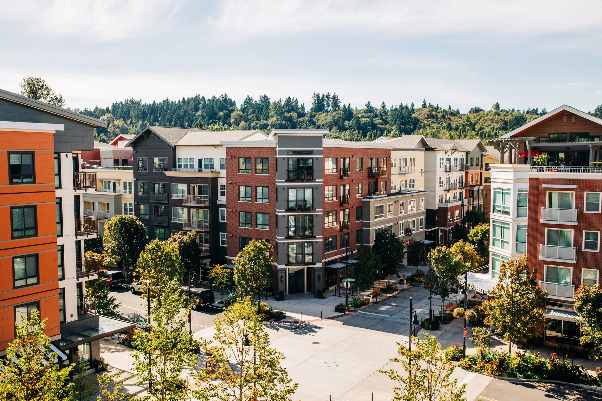 A modern apartment complex neighborhood with multi-story red brick and gray buildings surrounding a paved street.