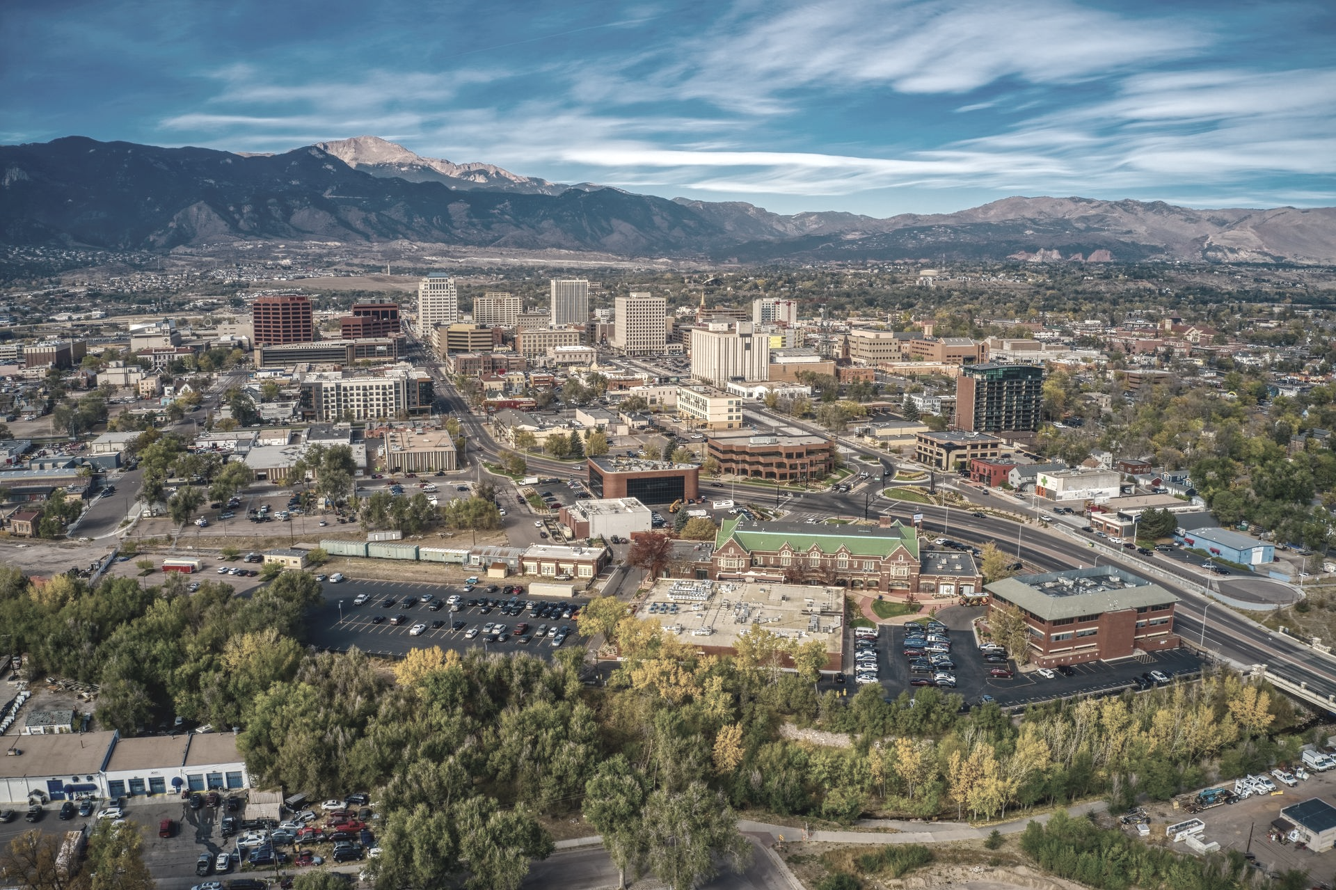 Aerial view of Colorado Springs, Colorado, featuring urban buildings with a large mountain range in the background.