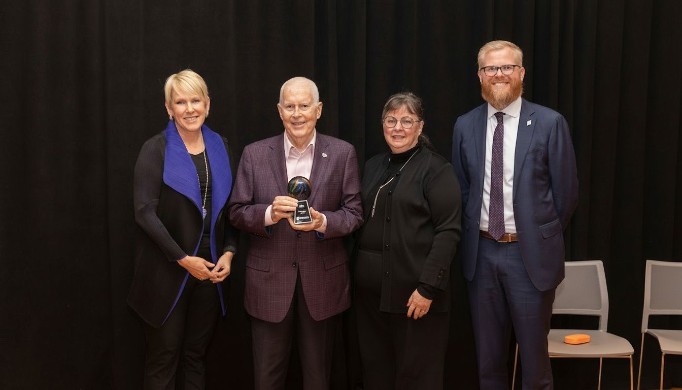 Four people stand in a line against a black backdrop. The second person from the left holds a small globe award.