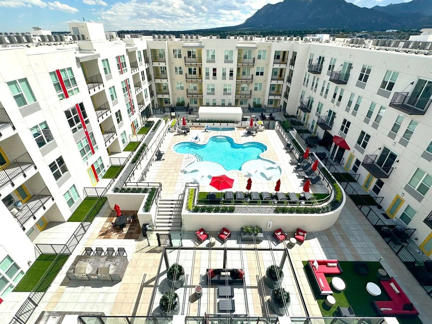 High-angle view of a modern apartment complex courtyard with a central pool, patio seating, and mountain backdrop.