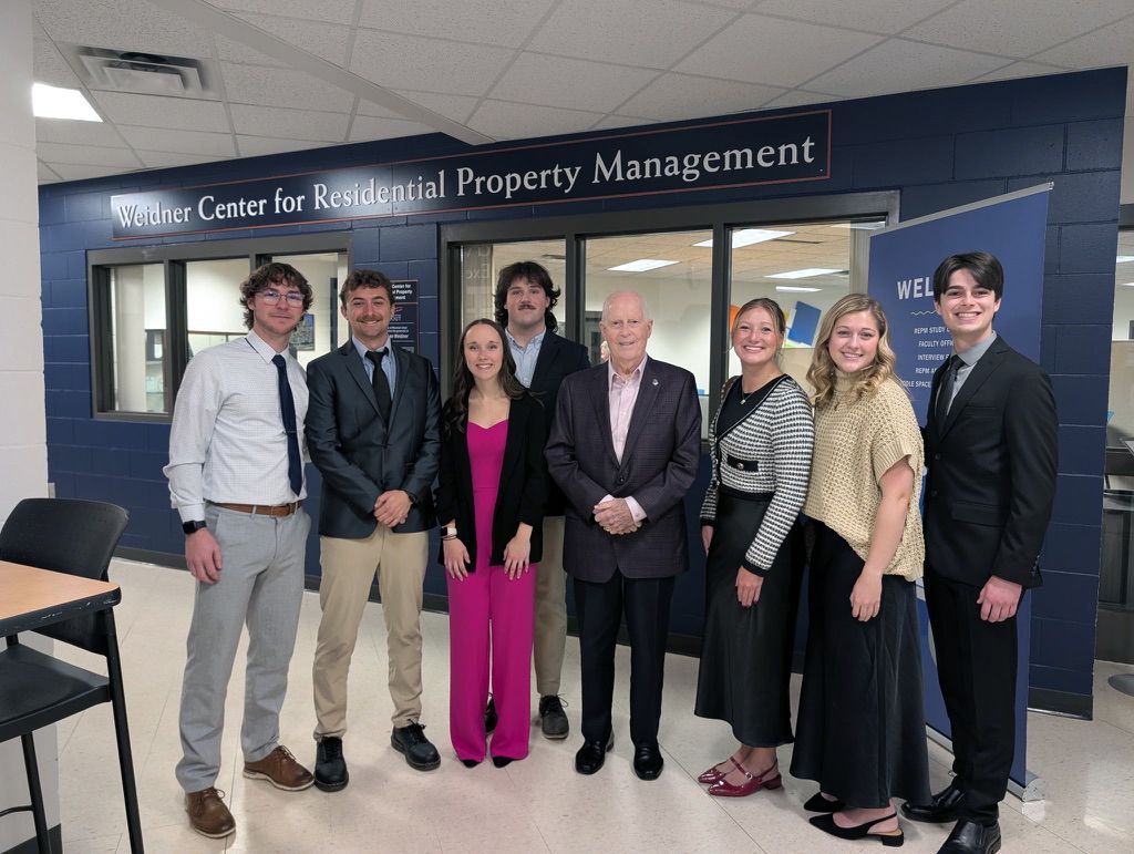 A group of eight people in business attire standing in front of the Center for Residential Property Management sign.