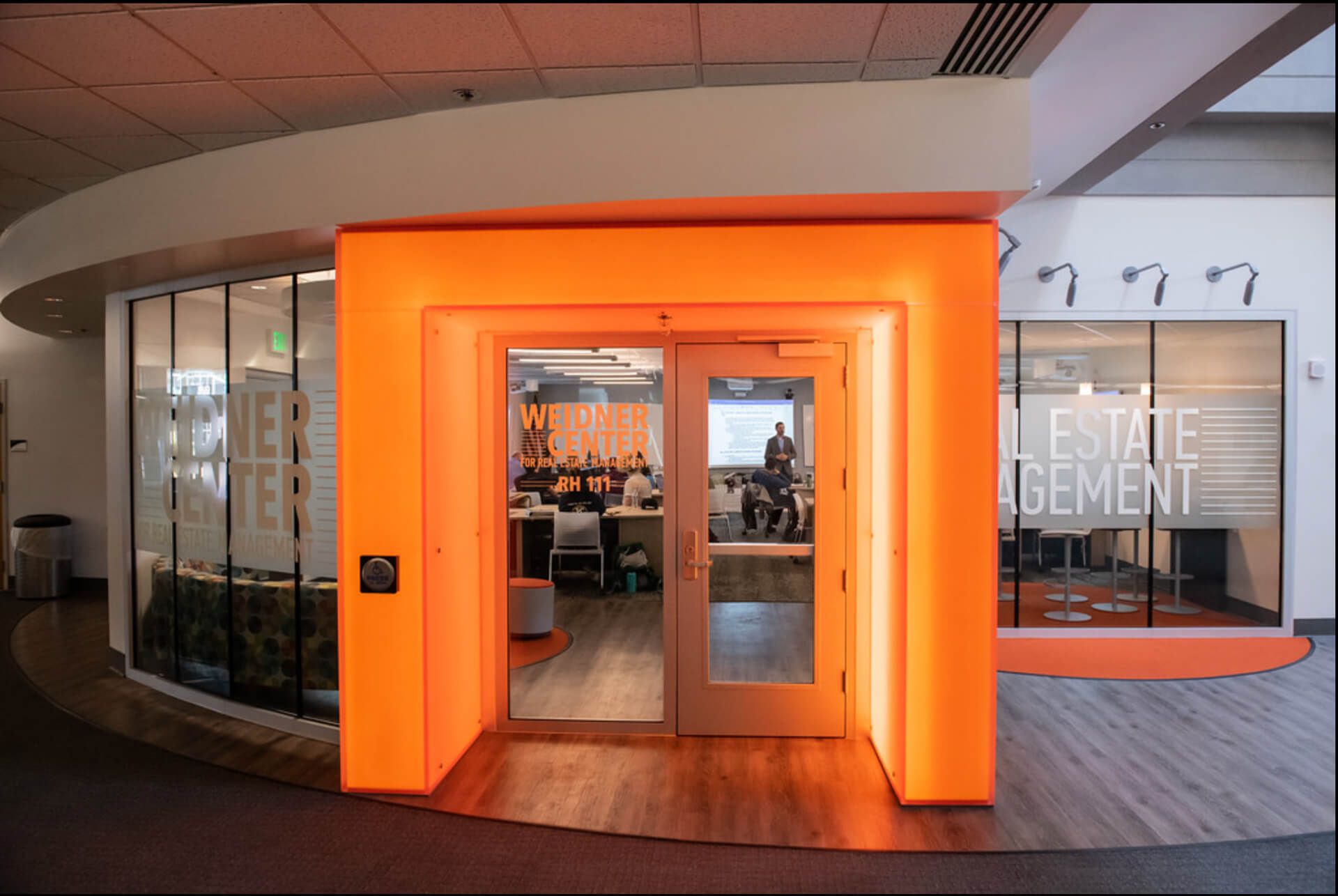 Bright orange, illuminated entrance leading into an office space with glass walls and professional meeting areas.