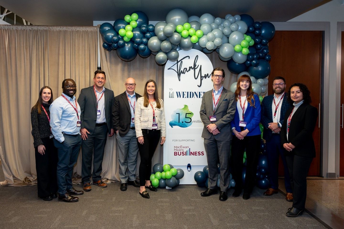 A group of professionals stands in front of a balloon arch and a banner celebrating a 15-year anniversary at an event.