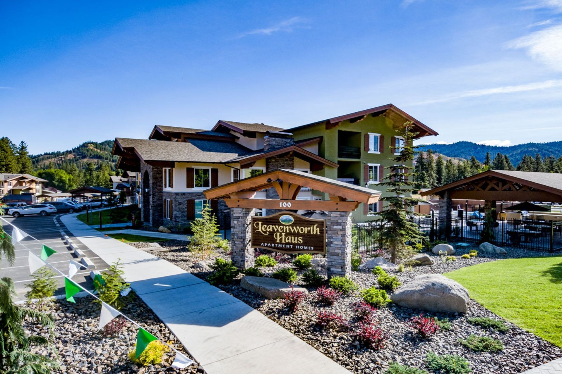 The Leavenworth Village Inn with a wooden sign, stone pillars, and green landscaping under a bright blue sky.