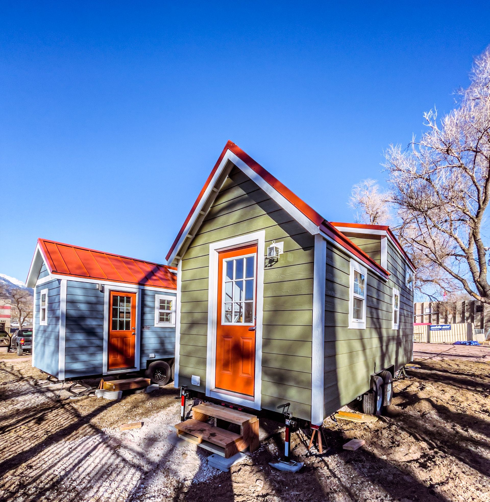 A row of small, colorful houses with red roofs arranged on a lawn with a clear blue sky in the background.