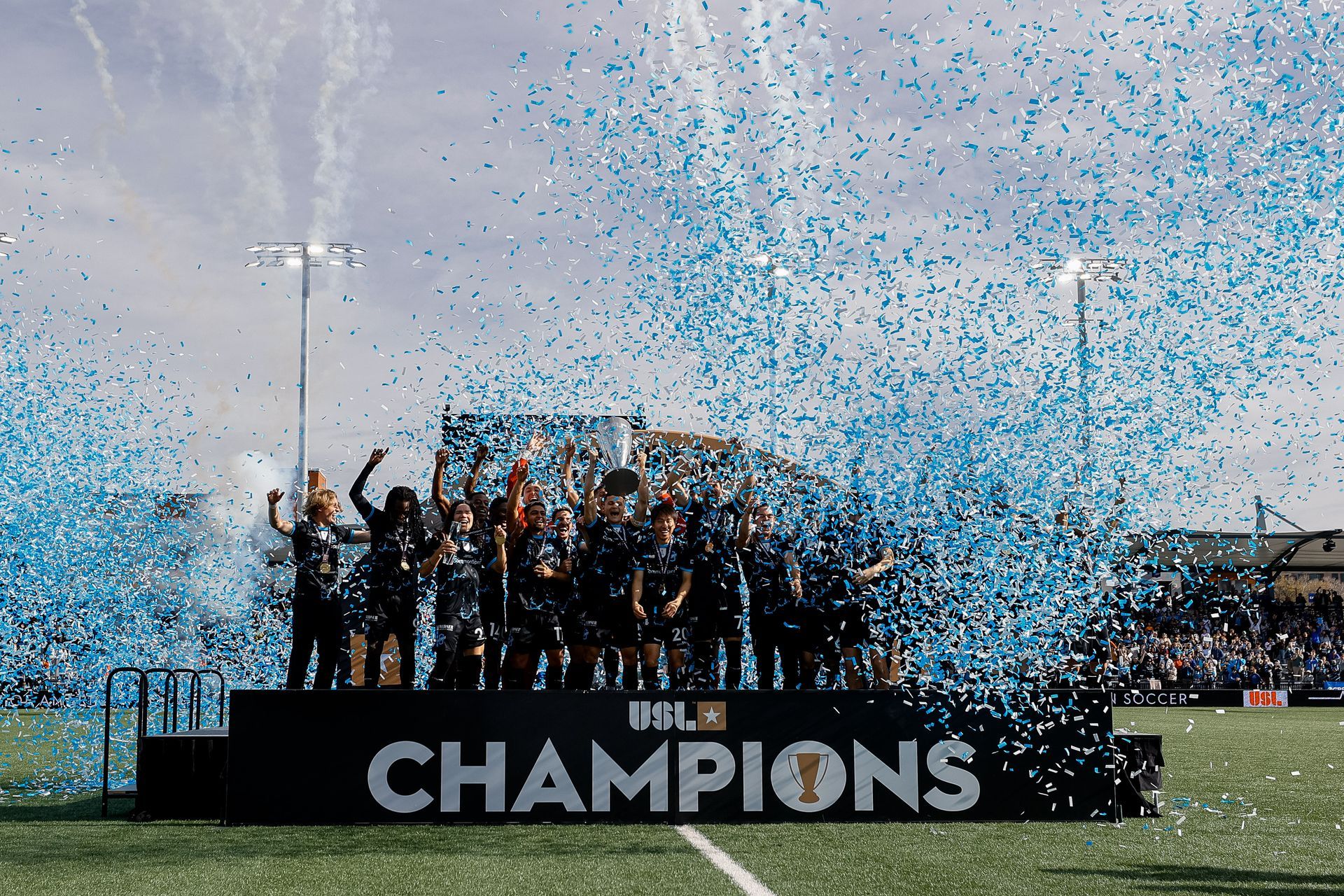 A low-angle, black-and-white view of a multi-story brick apartment building with a white van parked in the foreground.