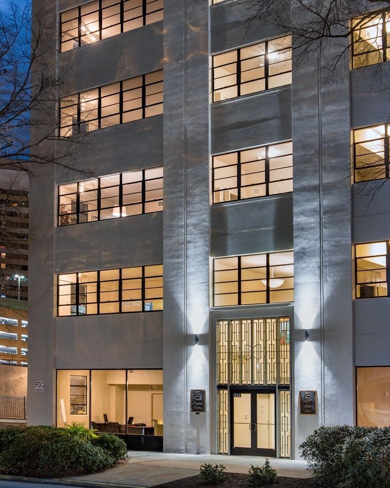 Office building facade at dusk with illuminated windows and lit entryway.