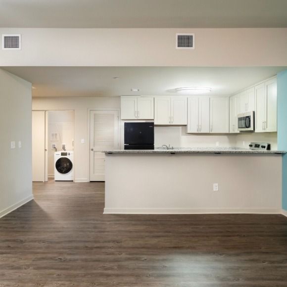 Open-concept apartment with kitchen, laundry, and dark wood floors; white cabinets and appliances.