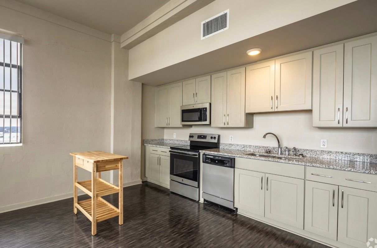 Kitchen with light-colored cabinets, stainless steel appliances, and wooden floors. A small wooden island sits on the left.