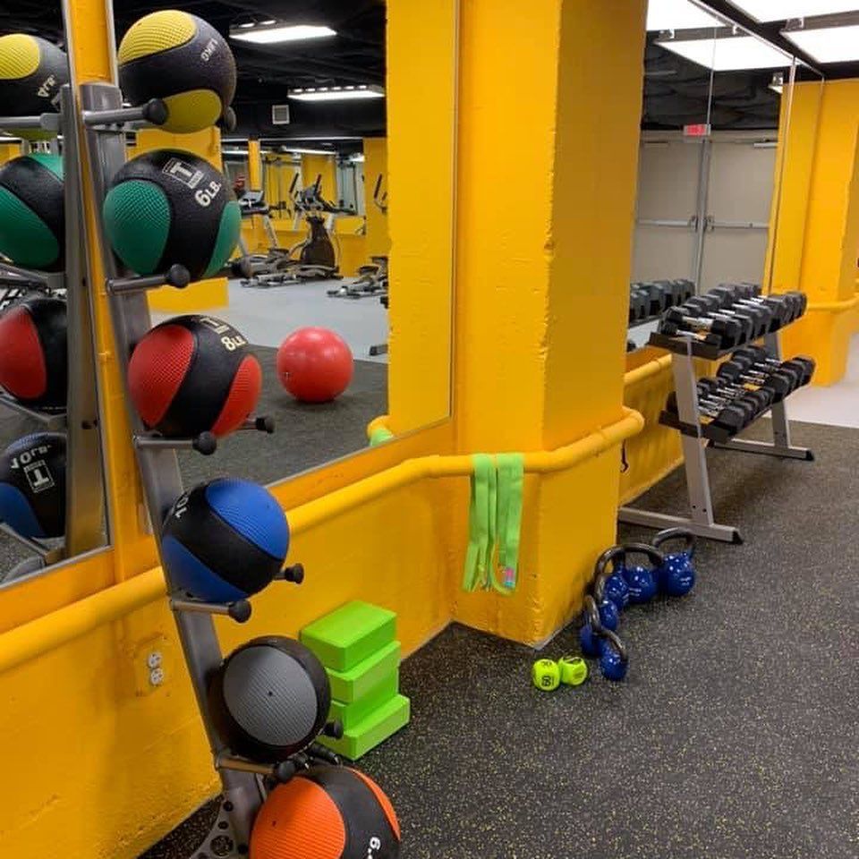 A gym with colorful medicine balls, dumbbells, and fitness equipment on a yellow and gray floor.