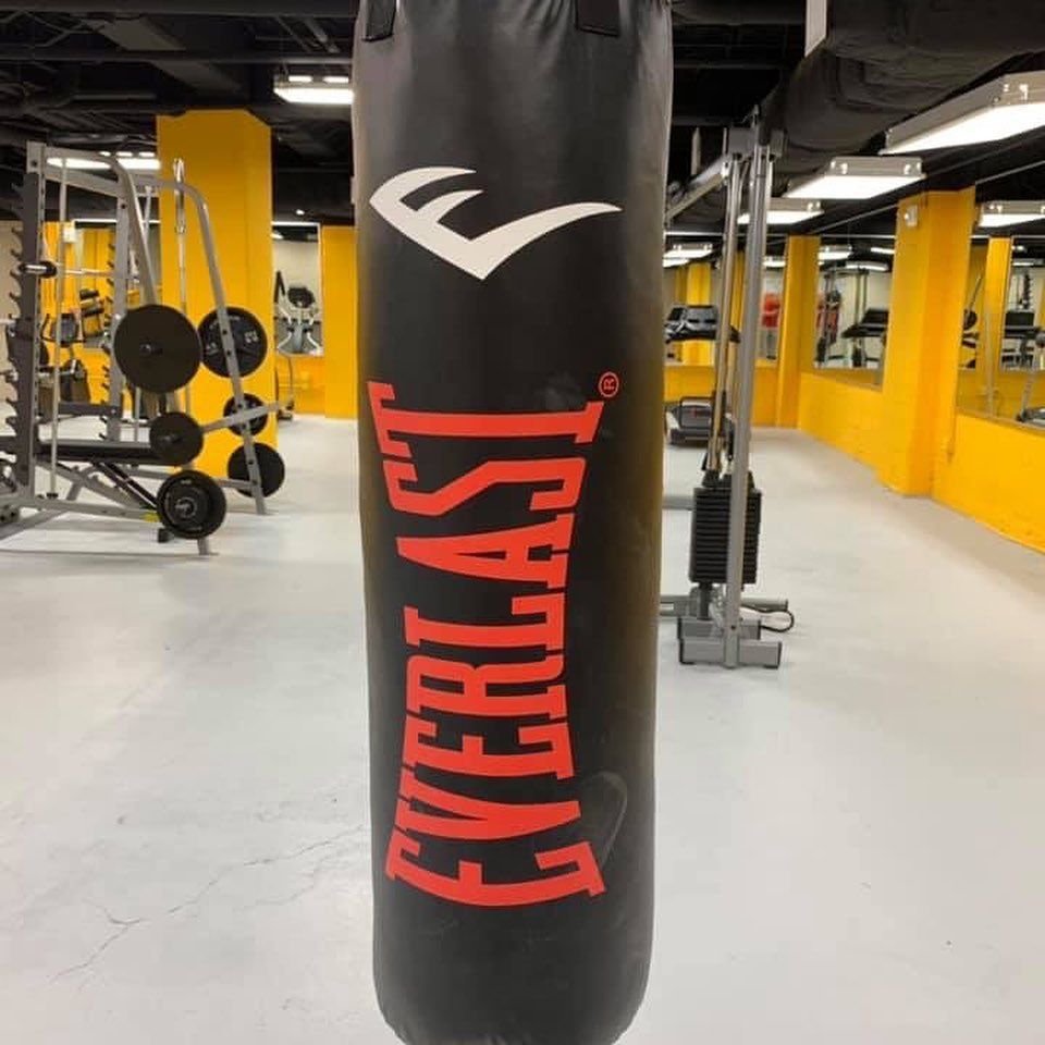 Black Everlast punching bag in a gym with yellow walls and exercise equipment.