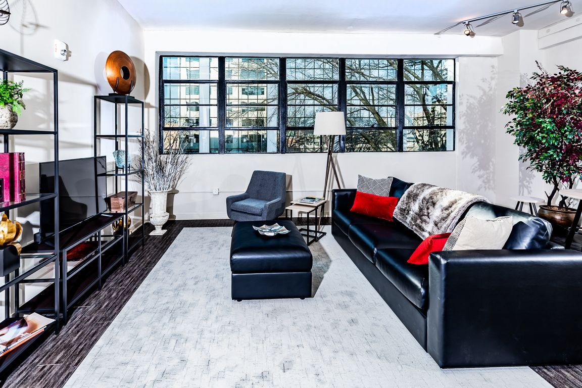 Living room with black leather sofa, large window, bookshelves, and rug.