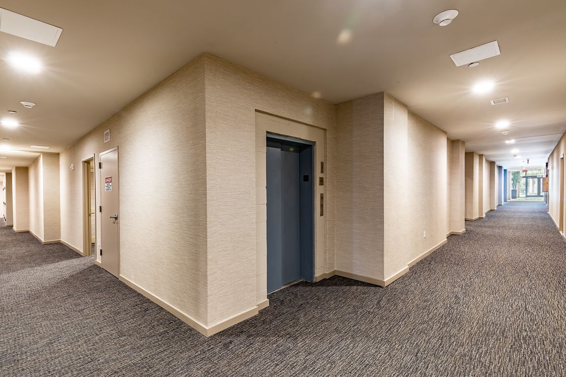 Hallway with elevator, textured walls, carpeted floors, and recessed lighting.