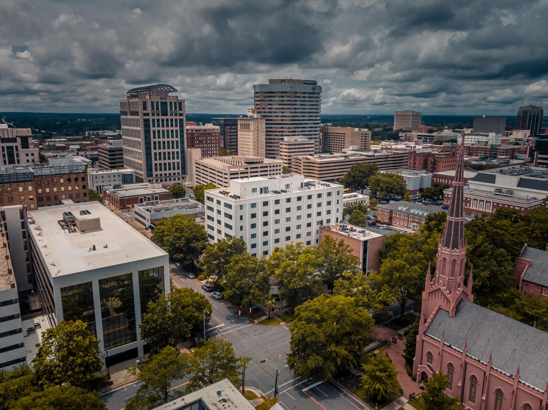 Aerial view of downtown Richmond, Virginia with high-rise buildings, trees, and a church under a cloudy sky.