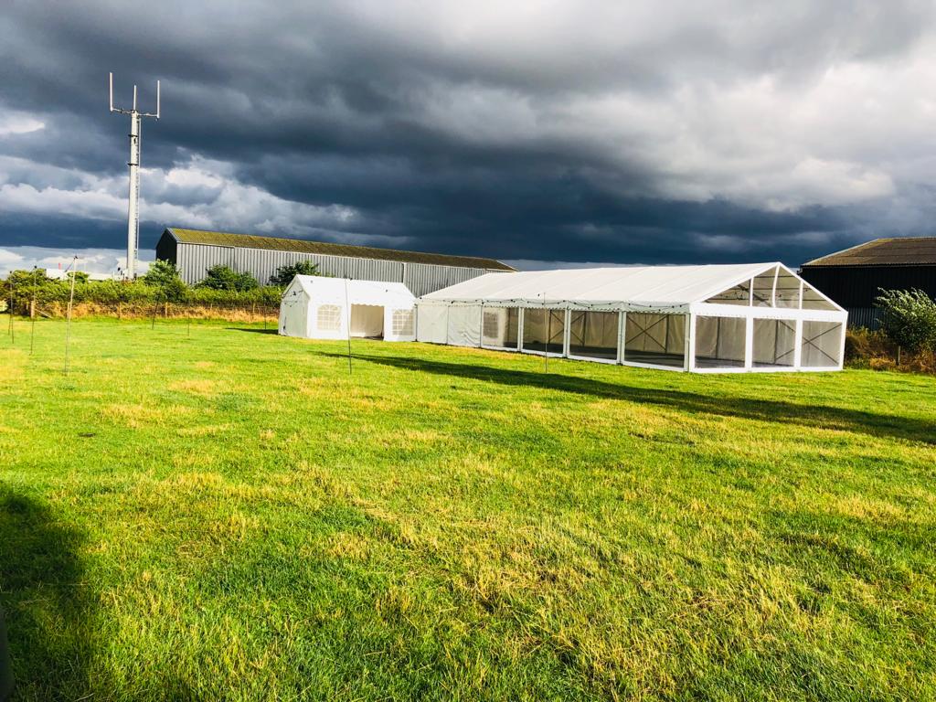 A row of tents are sitting in a grassy field under a cloudy sky.