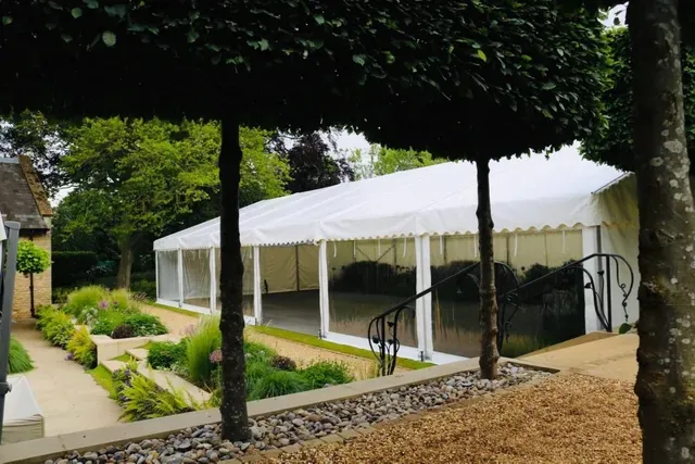 A large white tent is surrounded by trees in a garden