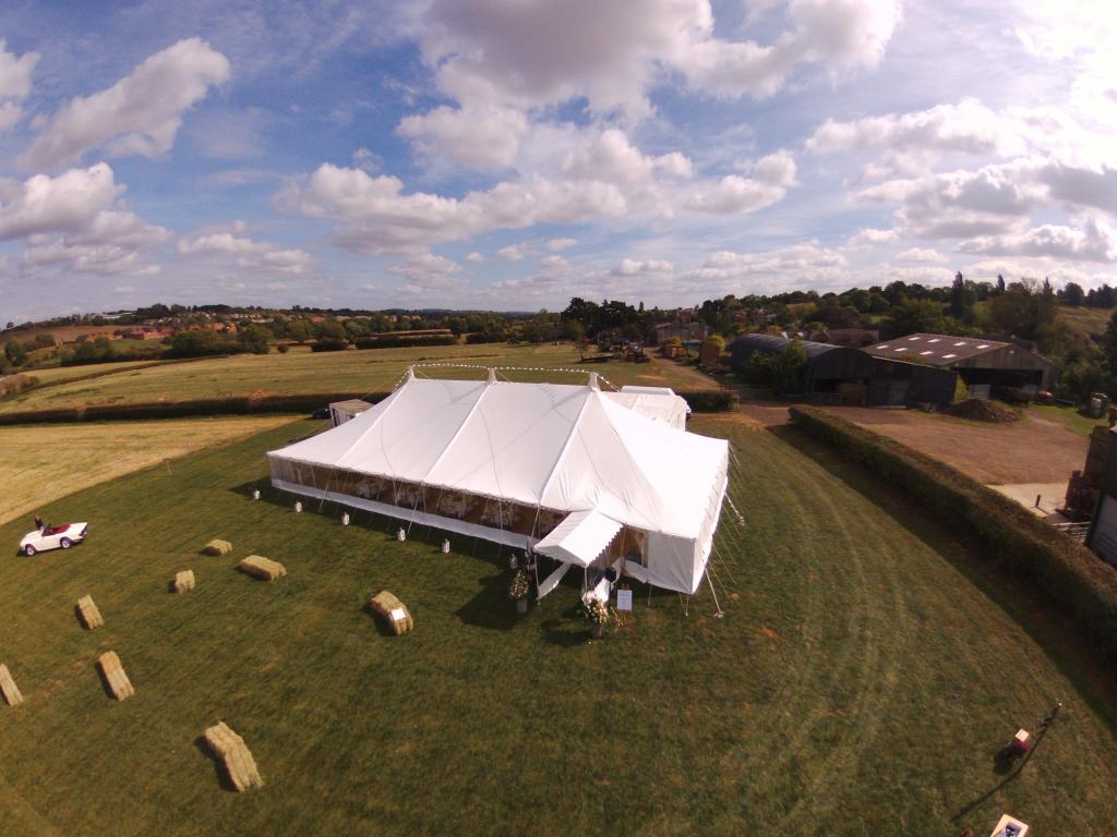 An aerial view of a large white tent in a grassy field.