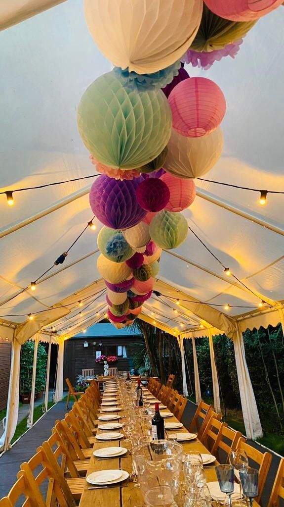 A long table with plates and glasses under a tent with lanterns hanging from the ceiling.