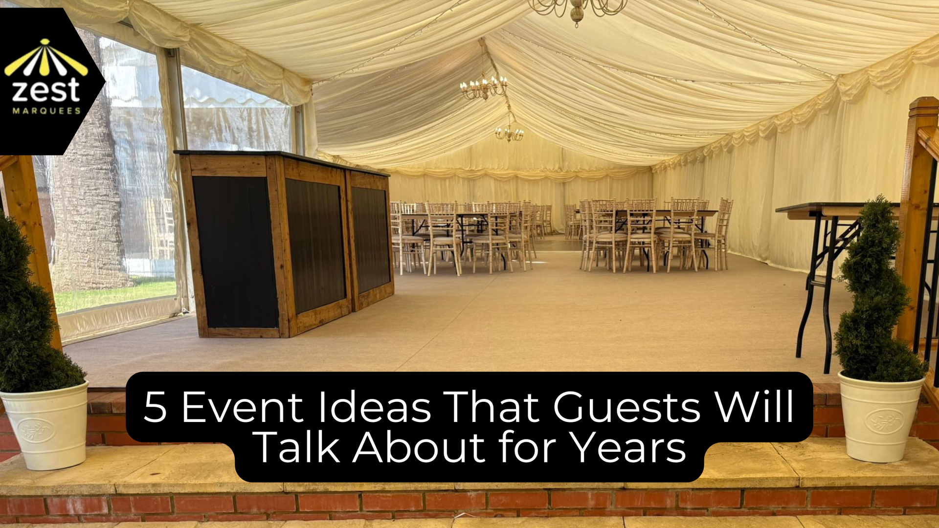 Decorated event tent with draped ceiling, tables, chairs, and stage setup under warm lighting