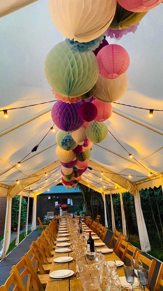 A long table with plates and glasses under a tent with lanterns hanging from the ceiling.