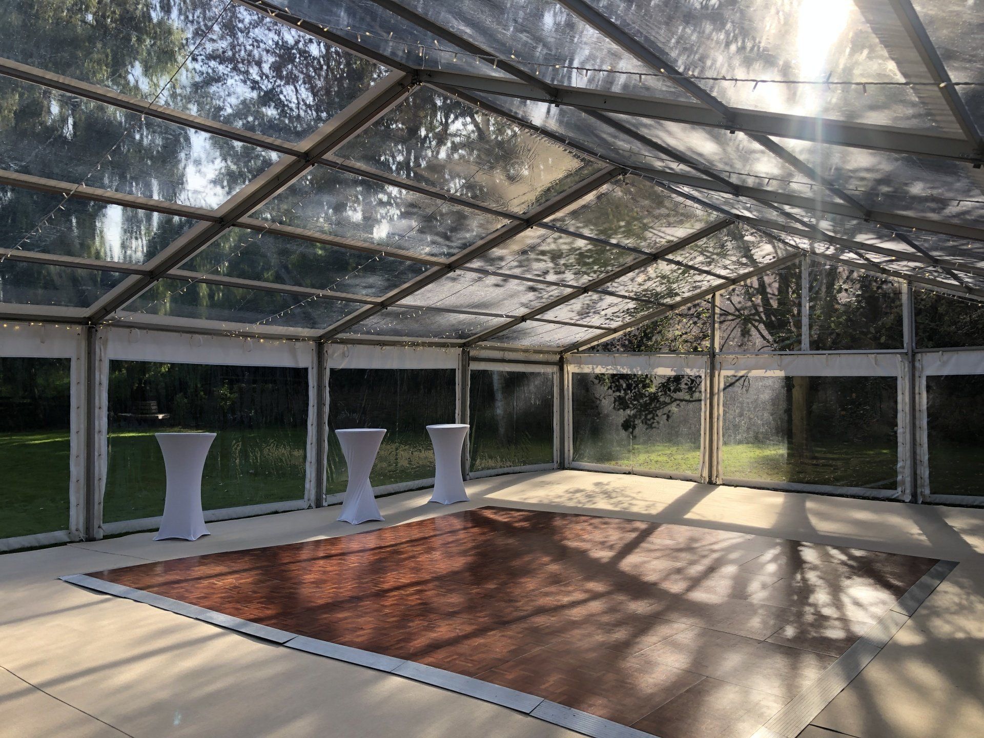 A clear tent with a wooden floor and tables underneath it.