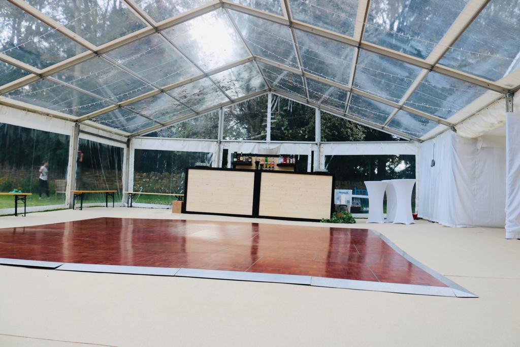 A clear tent with a wooden dance floor and a bar.