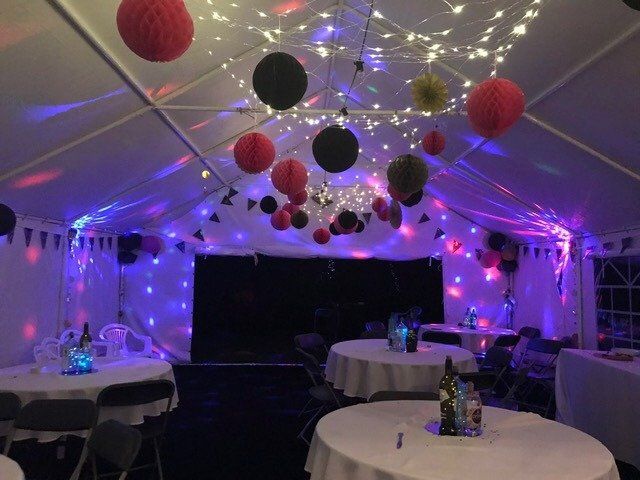 A tent is decorated with tables and chairs and lights.