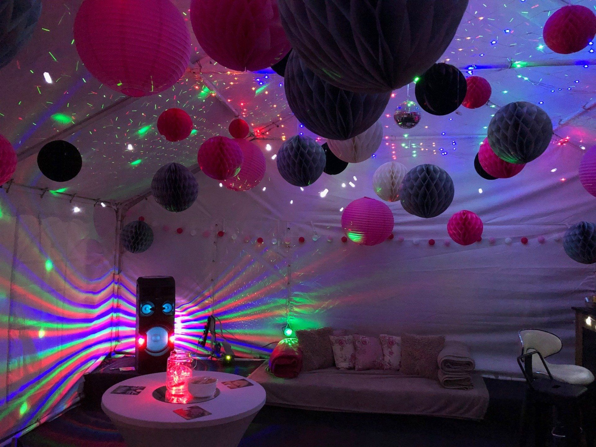 A room with a couch , table , speakers , and lanterns hanging from the ceiling.