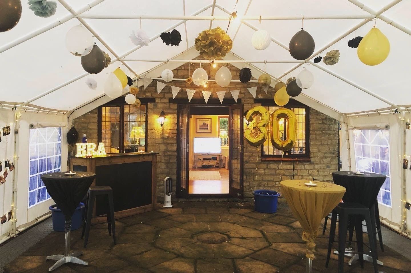 A tent is decorated with balloons and tables for a 30th birthday party.