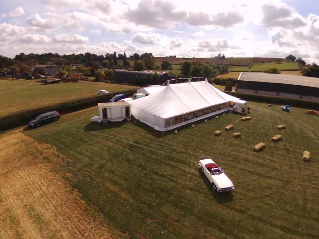 An aerial view of a large tent in a field with a car parked in front of it.