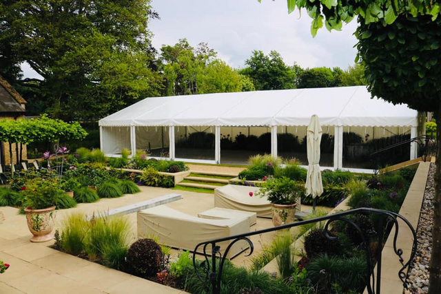 A large white tent is sitting in the middle of a garden.