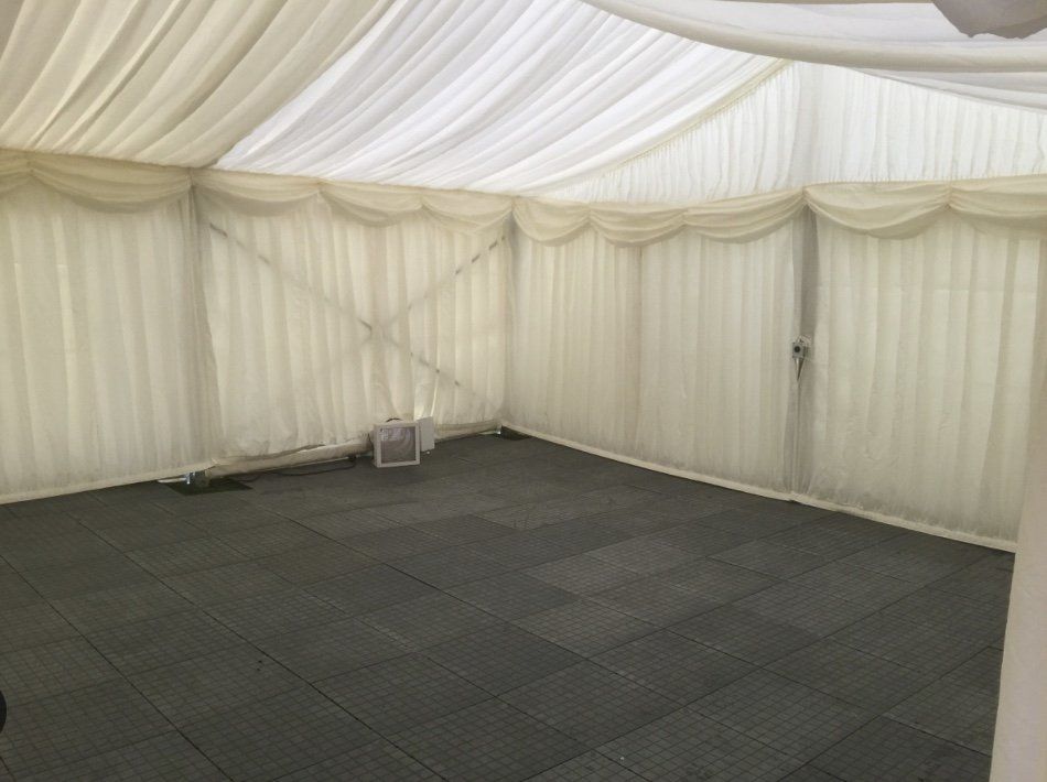 A large empty tent with a gray floor and white curtains.