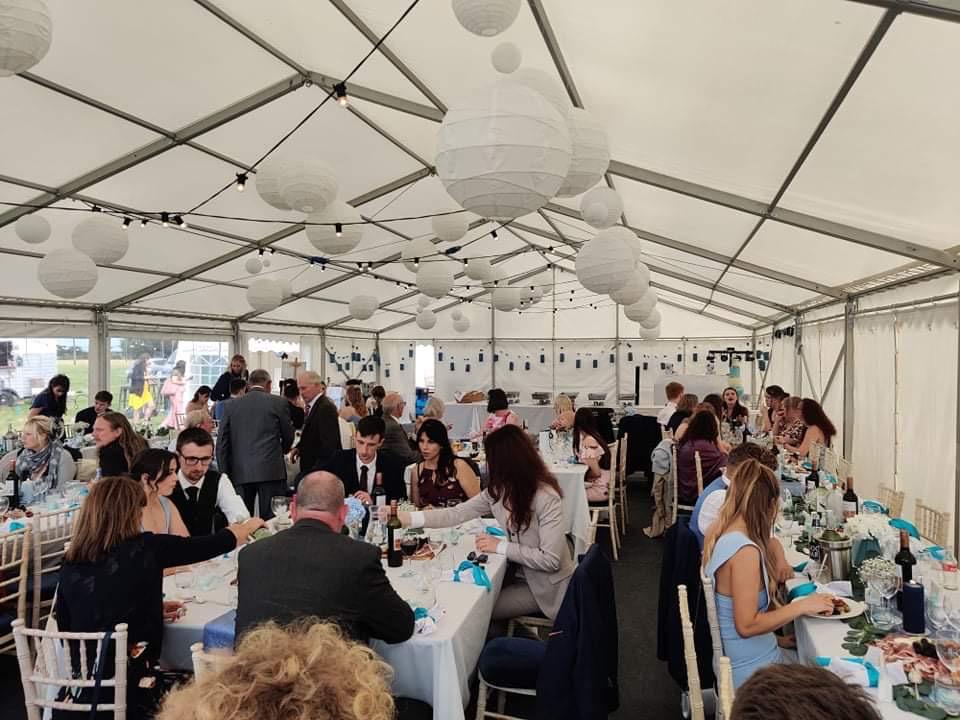 A large group of people are sitting at long tables in a tent.