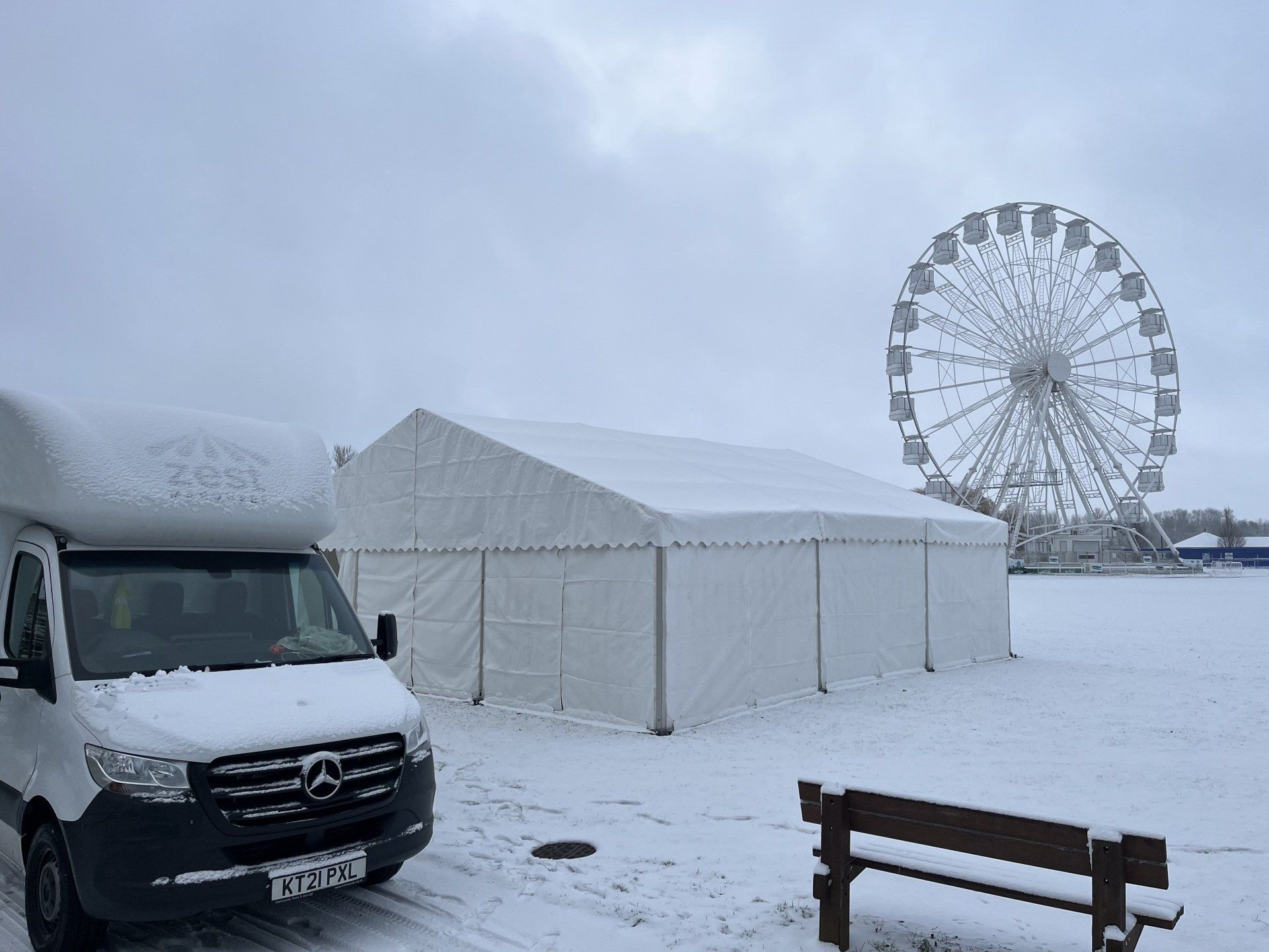 A van is parked in the snow in front of a ferris wheel.
