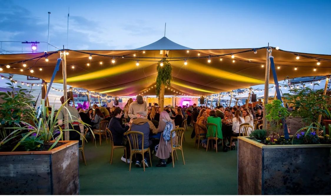 A large group of people are sitting at tables under a tent.
