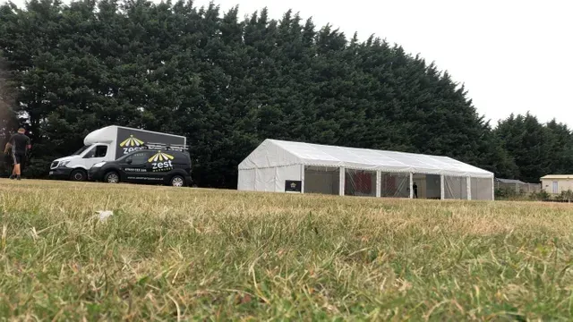 A white tent is sitting in the middle of a grassy field next to a van.