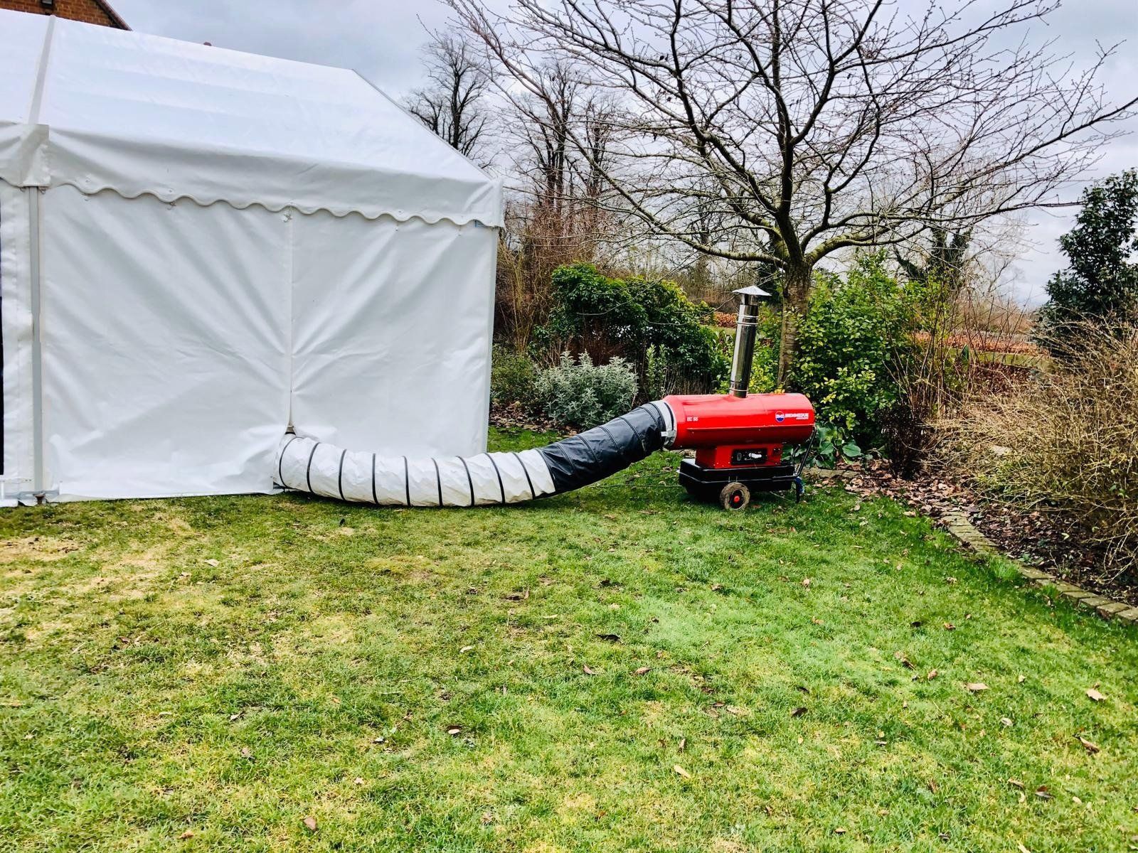 A red heater is sitting in the grass next to a white tent.