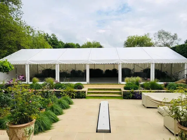 A large white tent is sitting in the middle of a garden.