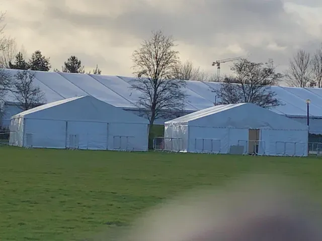 A group of white tents are sitting in a grassy field.