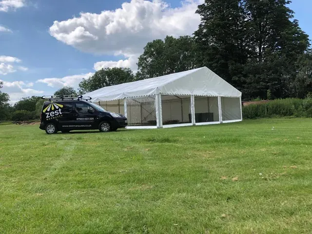 A black van is parked in front of a large white tent in a grassy field.