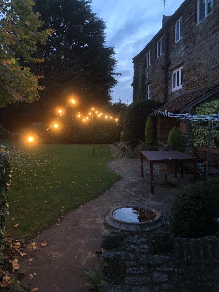 A row of lights are hanging from a pole in a garden.