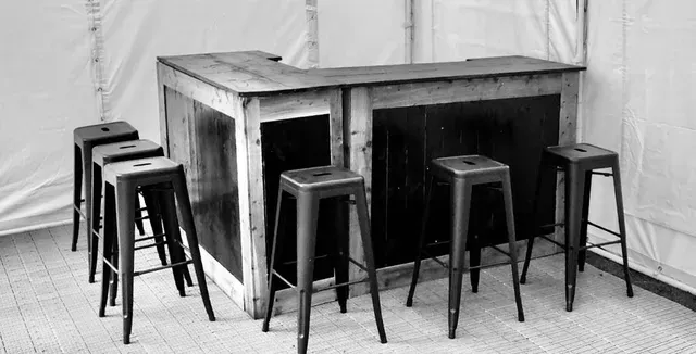 A black and white photo of a bar and stools in a tent.